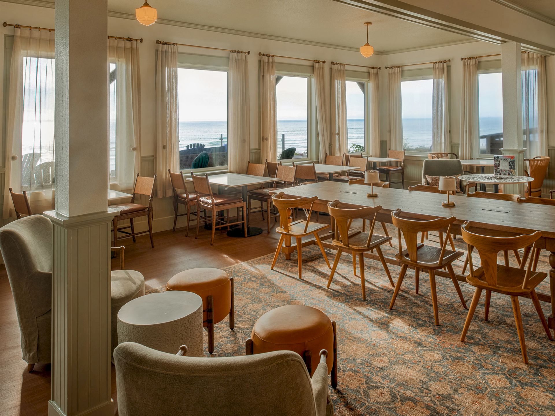 A cozy dining area with wooden chairs and tables, large windows offering a scenic ocean view, and soft lighting enhancing the ambiance.