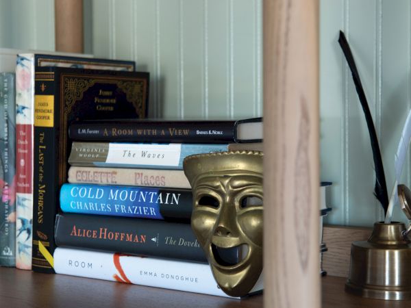 A bookshelf with various books, a gold theatrical comedy mask, and a quill pen in an inkpot.
