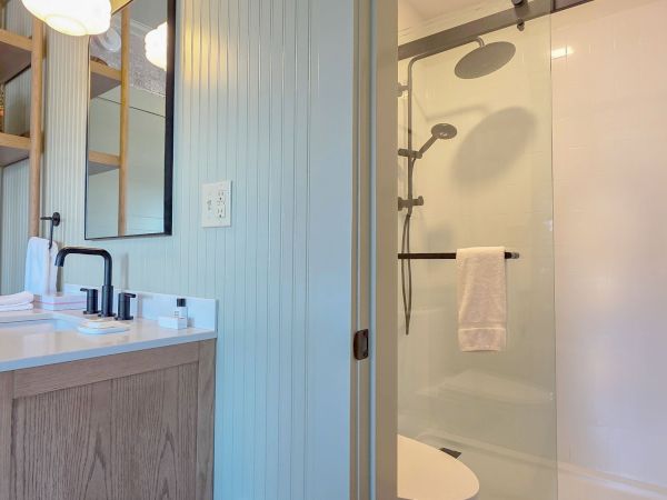 The image shows a modern bathroom with a wooden vanity, a sink, and a large glass shower enclosure.