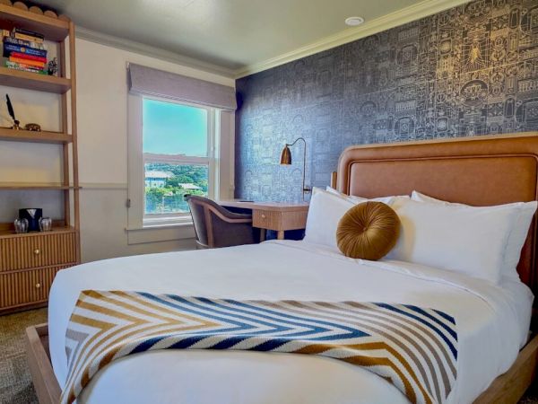 A cozy bedroom with a stylish bed, patterned accent wall, modern lamps, tall shelving, and a window view.