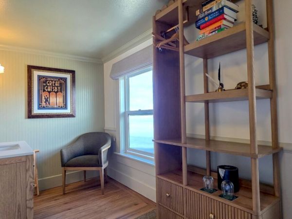 A cozy room with open shelves, books, a chair, a window, and a sink with a wall light.