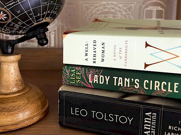 A globe on a wooden stand sits beside a stack of books, including Tolstoy and Lady Tanya&rsquo;s Circle, on a wooden shelf.