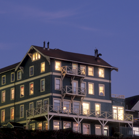A multi-story building with lit windows and balconies against a twilight sky.