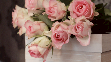 A bouquet of pink and cream roses in a white wooden box.