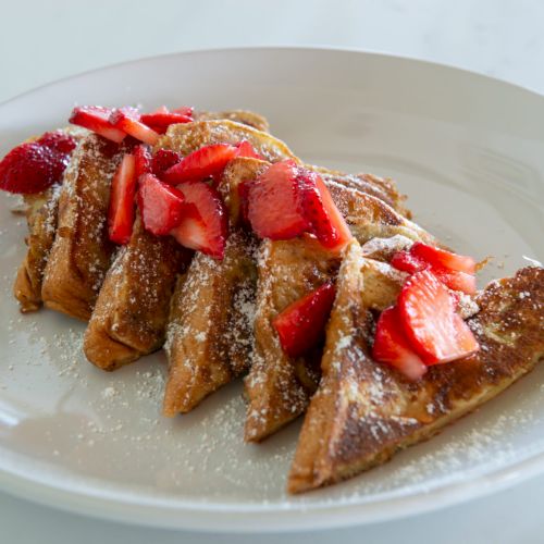 Sliced French toast topped with fresh strawberries and powdered sugar, arranged neatly on a white plate.