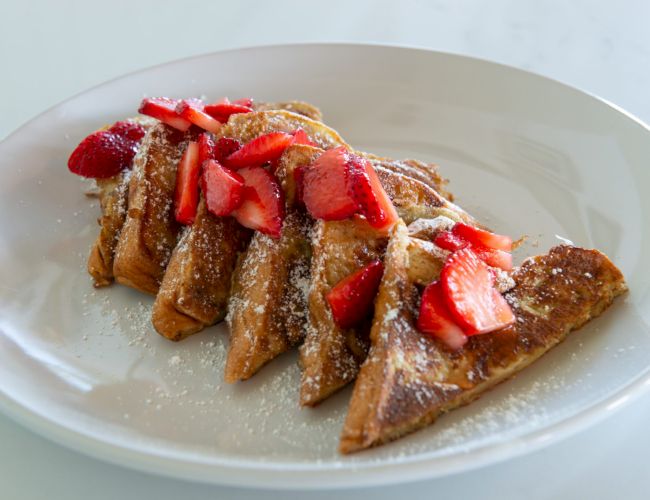 Sliced French toast topped with fresh strawberries and powdered sugar, arranged neatly on a white plate.