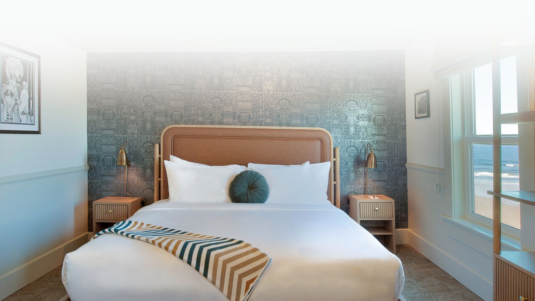 A bright, modern hotel bedroom with a large bed, white linens, a striped throw, two nightstands, and textured accent wall behind the headboard.