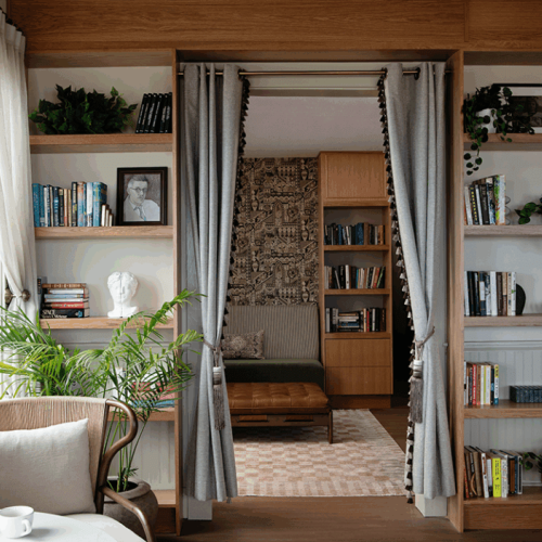 Cozy reading nook with a sofa, surrounded by bookshelves and decor, separated by curtains, plants, and art enhance the space.