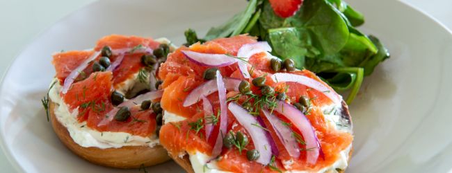 Two bagel halves topped with cream cheese, smoked salmon, red onion, capers, and herbs, served with a fresh greens salad on the side.