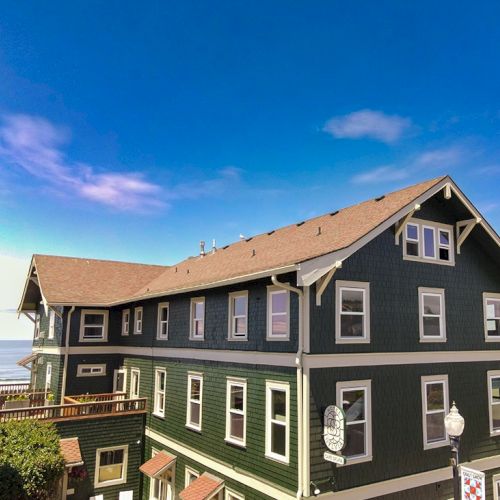 A green, multi-story seaside hotel with white trim and a brown roof, under a bright blue sky.